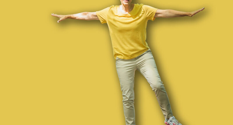 Balancing exercise outdoors. Mature woman standing on one leg, exercising balance