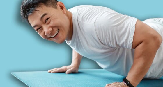 Active asian mature man standing in plank pose or doing push ups on mat at home and smiling at camera. Active korean male leading active lifestyle, exercising indoors