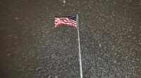 A flag ripples in the wind as snow falls in Lowville, New York, on Tuesday night, Dec. 9, 2025. The area faces a winter storm warning through Thursday. (AP Photo/Cara Anna)