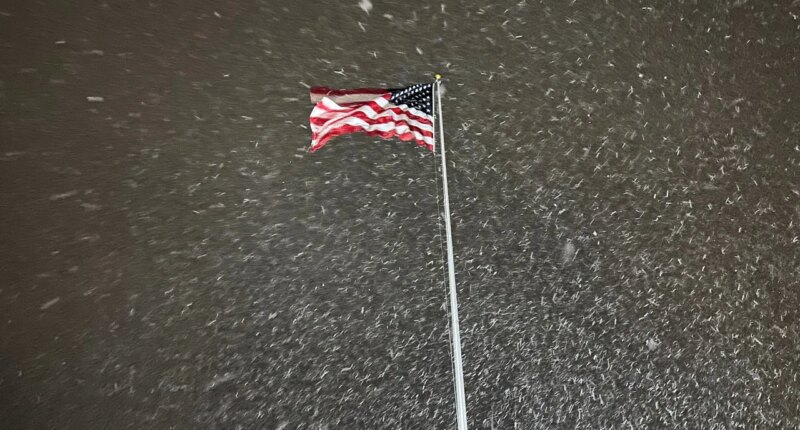 A flag ripples in the wind as snow falls in Lowville, New York, on Tuesday night, Dec. 9, 2025. The area faces a winter storm warning through Thursday. (AP Photo/Cara Anna)