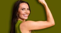 Confident young woman smiling and flexing her arm against a bright yellow background, symbolizing strength, positivity, and cheerful energy.