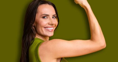 Confident young woman smiling and flexing her arm against a bright yellow background, symbolizing strength, positivity, and cheerful energy.