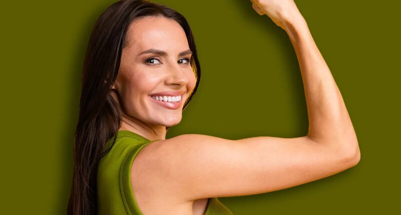 Confident young woman smiling and flexing her arm against a bright yellow background, symbolizing strength, positivity, and cheerful energy.