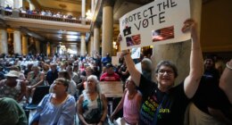 FILE - Annette Groos holds a sign before the start of a rally featuring former Transportation Secretary Pete Buttigieg at the Statehouse in Indianapolis, Thursday, Sept. 18, 2025 for Indiana Democrats amid pressure from President Donald Trump on Republicans who control the state