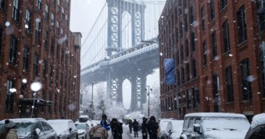 People gather on Washington Street in front of Manhattan Bridge during a snowfall, Sunday, Dec. 14, 2025, in the Brooklyn Borough of New York. (AP Photo/Adam Gray)