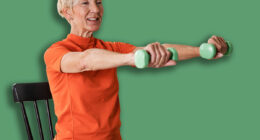 Smiling beautiful senior woman health instructor doing chair exercises with dumbbells