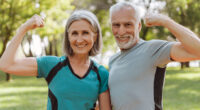 Smiling, attractive senior athletic couple flexing muscles in park, looking at camera outdoors, active lifestyle concept