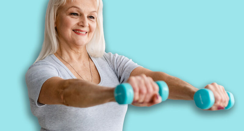 Home Physiotherapy Concept. Portrait Of Smiling Active Senior Lady Exercising With Two Dumbbells In Living Room, Enjoying Workout. Free Copy Space, Blurred Background, Selective Focus