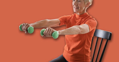 Smiling beautiful senior woman health instructor doing chair exercises with dumbbells