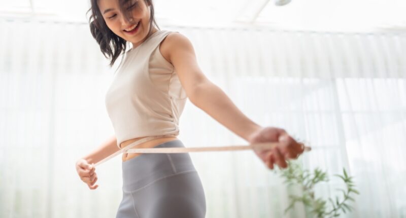 Young Asian woman in sportswear measuring her waist with a tape. Diet and healthy concept. Body shape slim