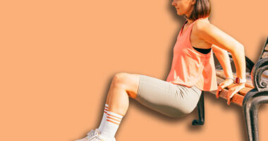Vertical outdoors shot of a fit woman exercising her triceps on a park bench.
