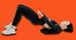 Sporty woman doing glute bridge exercise with orange dumbbells on white background. Concept of fitness, strength training, workout routine, and healthy lifestyle.