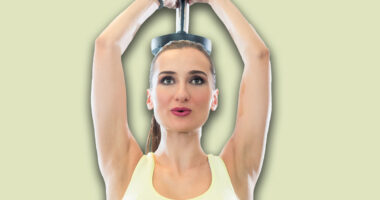 Portrait of a beautiful fit woman with can do attitude exercising triceps extension with dumbbell during workout in a modern fitness club