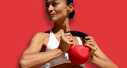 Athletic woman in white sports bra and blue shorts holding red k