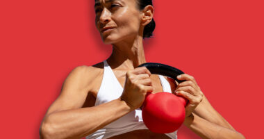 Athletic woman in white sports bra and blue shorts holding red k