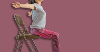 Full length shot of energetic mature woman making exercising and practicing restorative yoga on mat and chair at home because of social distancing, wearing sports clothes.