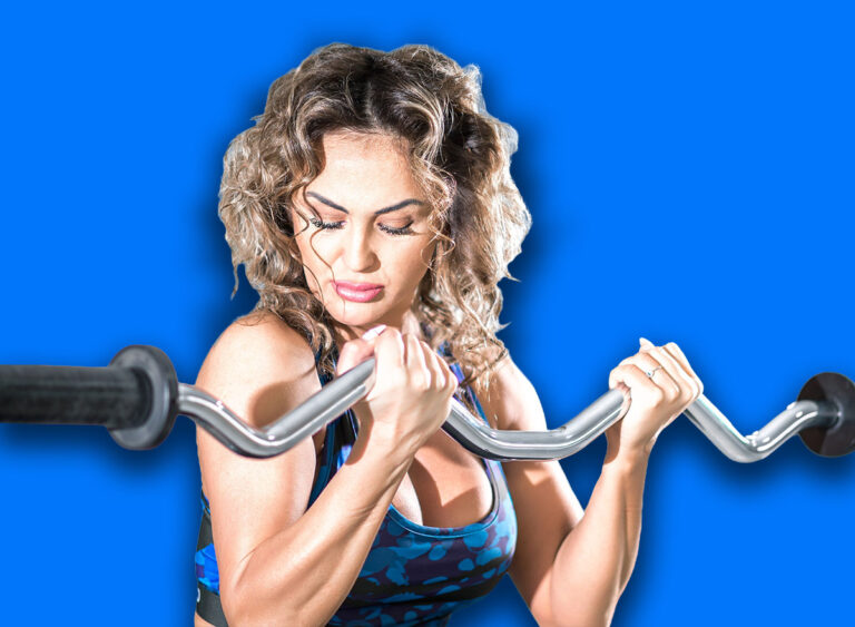 Attractive woman with curly hair doing preacher curl biceps exercise on bench with EZ curl bar in modern fitness center. Toned image.
