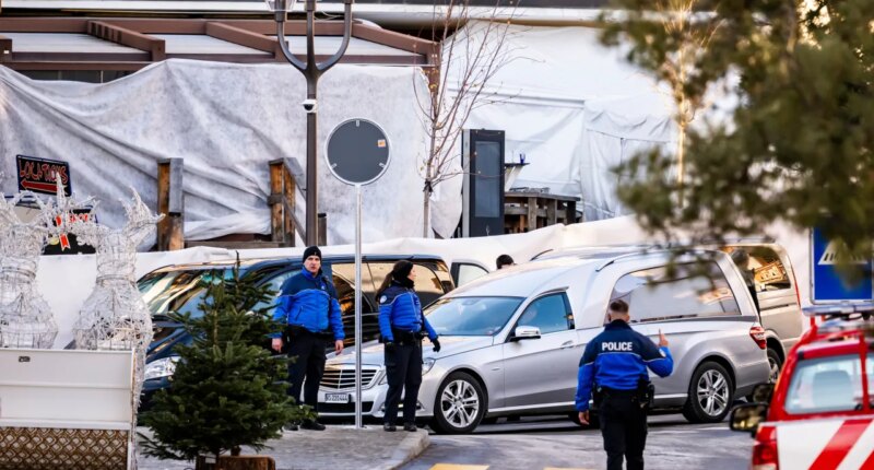 A hearse drives past as police officers inspect the area where a fire broke out at the Le Constellation bar and lounge during New Year