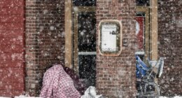 Two people take cover in an entryway of a downtown restaurant on Fourth Avenue, Thursday, Nov. 9, 2023 in Anchorage, Alaska. Four homeless people have died in Anchorage in the last week, underscoring the city’s ongoing struggle to house a large houseless population at the same time winter weather has returned, with more than 2 feet (0.61 meters) of snow falling within 48 hours. (Marc Lester/Anchorage Daily News via AP)