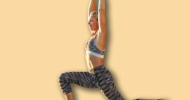 Adult woman lunges while holding arms above her head and warming up for sports training near the sea beach.