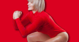 Sporty Caucasian woman practicing squat exercises in studio. Mature muscular woman in red sportswear bodysuit working out on white background. Sport and healthy lifestyle. Strength and motivation.