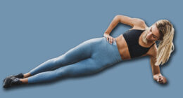 Young fit woman doing side plank while exercising outdoors, on riverside city promenade.