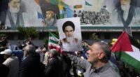 Iranian worshippers walk past a mural showing the late revolutionary founder Ayatollah Khomeini, right, Supreme Leader Ayatollah Ali Khamenei, left, and Basij paramilitary force, as they hold a poster of Ayatollah Khomeini and Iranian and Palestinian flags in an anti-Israeli gathering after their Friday prayer in Tehran, Iran, Friday, April 19, 2024.