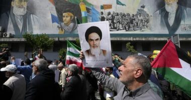 Iranian worshippers walk past a mural showing the late revolutionary founder Ayatollah Khomeini, right, Supreme Leader Ayatollah Ali Khamenei, left, and Basij paramilitary force, as they hold a poster of Ayatollah Khomeini and Iranian and Palestinian flags in an anti-Israeli gathering after their Friday prayer in Tehran, Iran, Friday, April 19, 2024.
