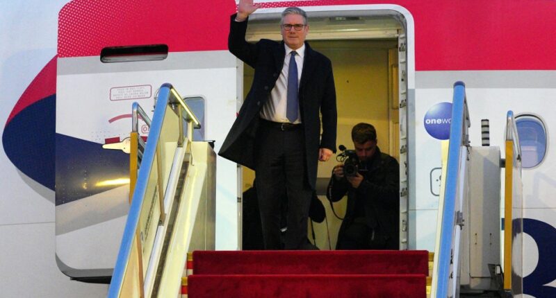 British Prime Minister Keir Starmer waves from the top of an airplane's red-carpeted stairs.
