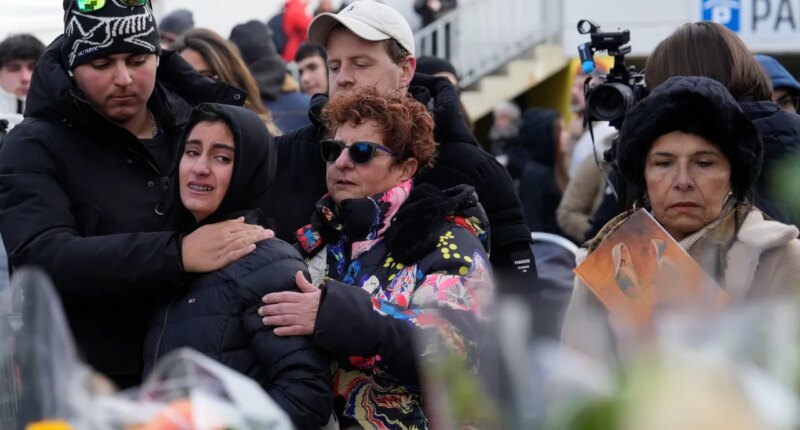People mourn behind flowers near the sealed off Le Constellation bar, where a devastating fire left dead and injured during the New Year