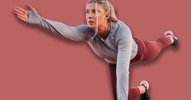 Young woman passionate about sports exercises outdoors on a running track, listening to music and focusing on her bird dog exercise, showcasing dedication to a healthy lifestyle