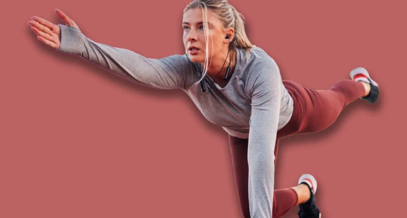 Young woman passionate about sports exercises outdoors on a running track, listening to music and focusing on her bird dog exercise, showcasing dedication to a healthy lifestyle