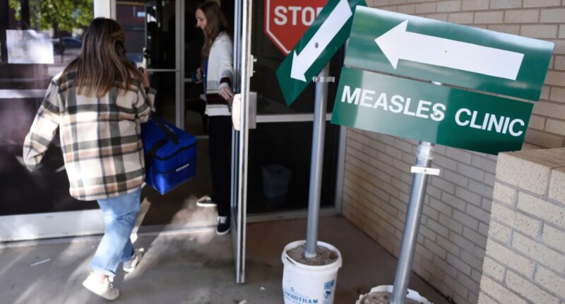 FILE - Health department staff members enter the Andrews County Health Department measles clinic carrying doses of the measles, mumps and rubella vaccine, Tuesday, April 8, 2025, in Andrews, Texas. (AP Photo/Annie Rice, File)