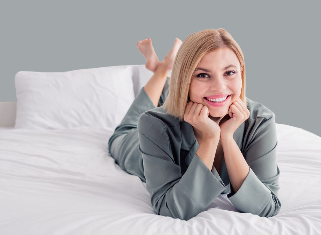 Closeup photo of pretty woman blonde model wear brand pajama cozy clothes nightwear to sleep touch cheek lying down soft white bed