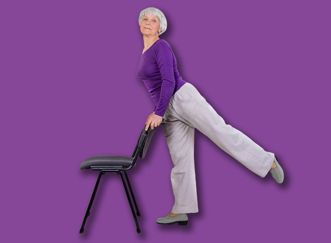 Happy charming beautiful elderly woman is doing exercise on a chair. Exercising gymnastics for health in the fitness room. Sports training.