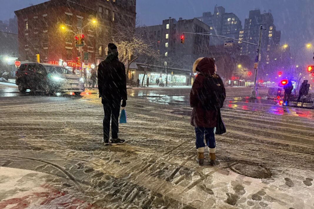People wait to cross the corner of 20th Street and First Ave. during a snowstorm, Sunday, Feb. 22, 2026, in New York. (AP Photo/Pamela Hassell)