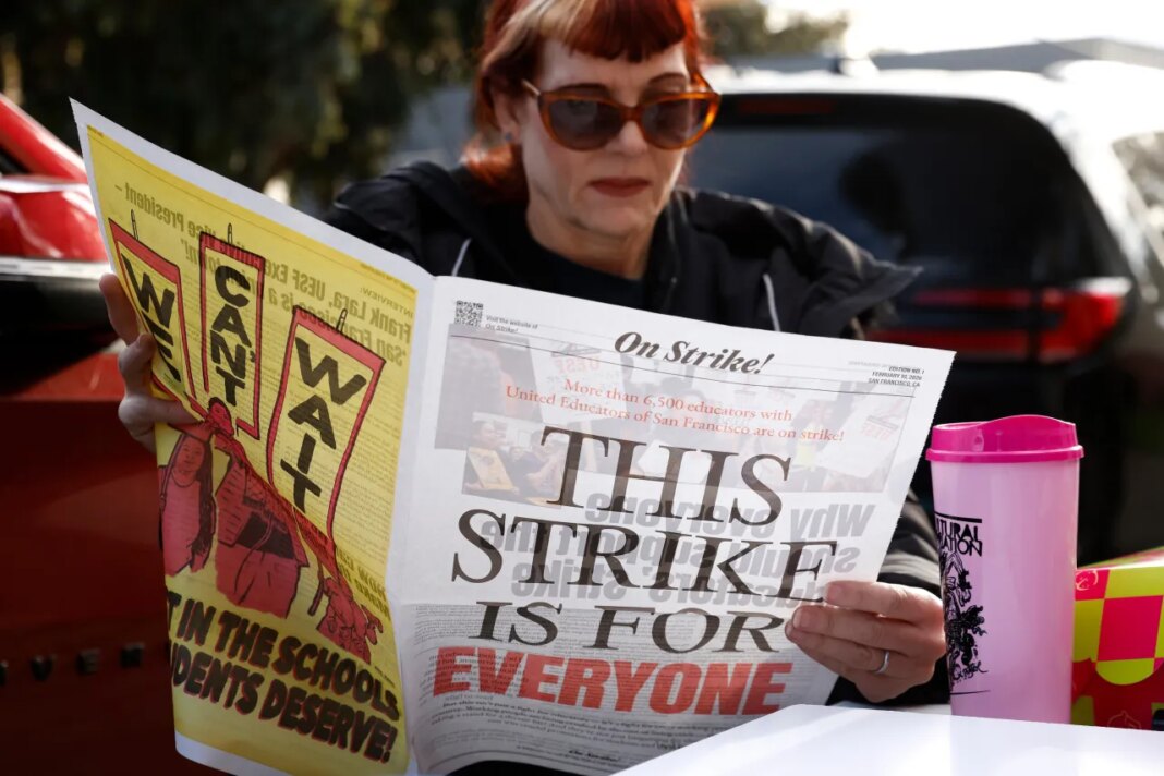 Bret Harte Elementary Stacey Gonzalez TK teacher reads a United Educators of San Francisco newspaper as Bret Harte Elementary School teachers and Untied Educators of San Francisco members strike outside of Bret Harte Elementary School in San Francisco, Calif., Tuesday, Feb. 10, 2026. (Jessica Christian/San Francisco Chronicle via AP)