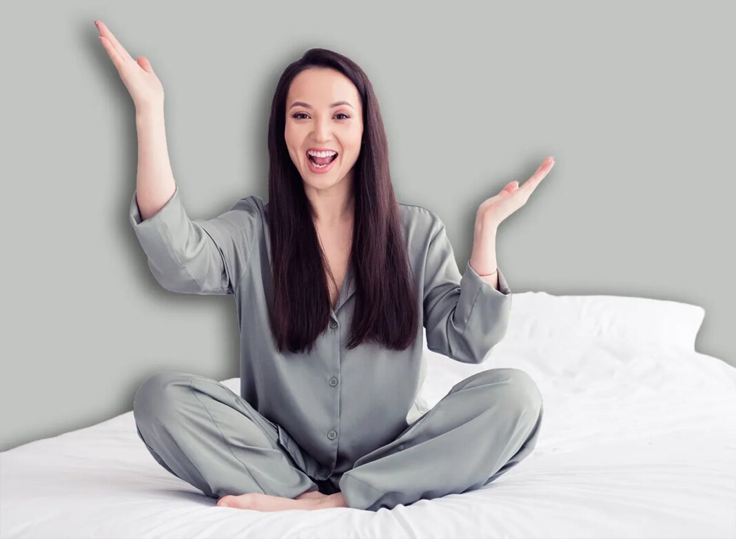Photo portrait of attractive young woman sit soft bed raise hands excited wear trendy gray pajama isolated on white modern interior design