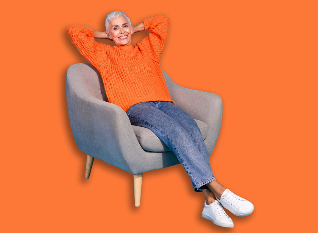 Photo of positive old lady sit chair relax hold hands over head isolated blue color background