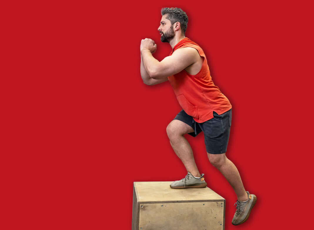 Man in sportswear doing step up workout with wooden box in crossfit gym.