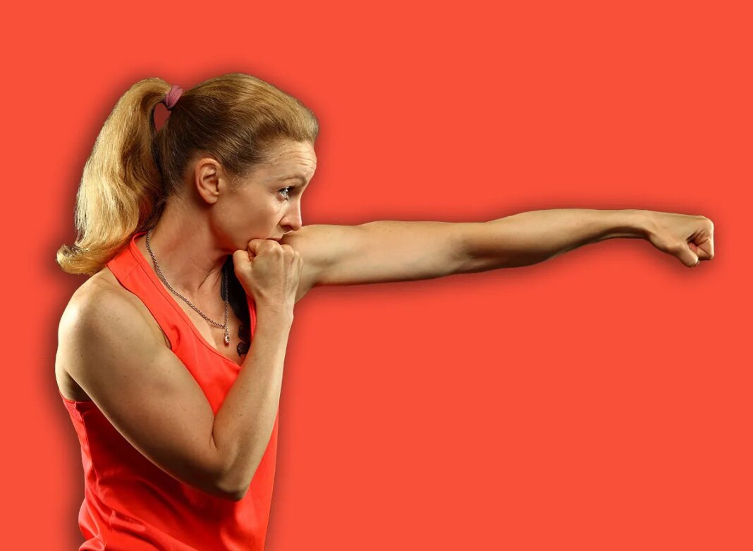 Close up side view profile portrait of one young middle age athletic woman shadow boxing in sportswear in gym over dark background, looking away