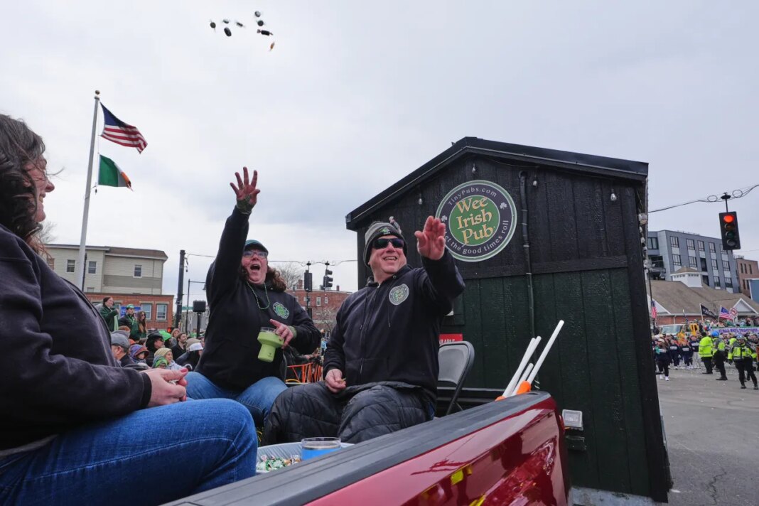 Dena Taylor and Tony DiDonato, right, toss candy to spectators while riding in a truck hauling the "Wee Irish Pub", a fully functioning mobile Irish pub built by two Massachusetts