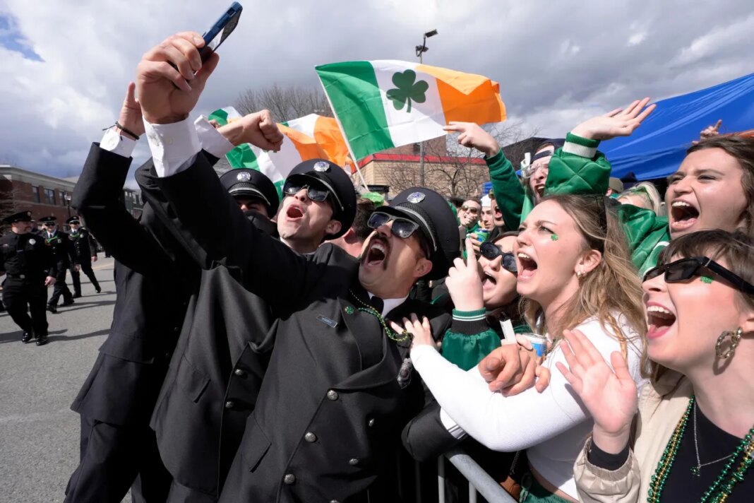 FILE - A group of firemen from around the United States pose for a selfie with spectators while marching in the St. Patrick