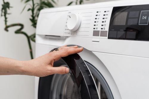 Cropped view of woman open or close door at automatic washing machine with settings on digital display and modern control panel. Laundry at home and daily housework routine concept