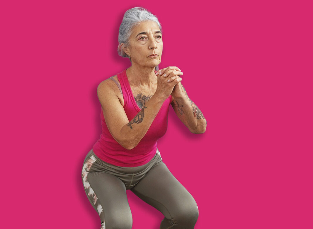 Grey-haired woman exercising at gym performing squats in an indoor sport center with gym equipment visible in the background