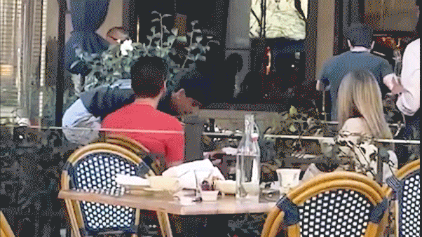 Two men appear to shove and lunge toward each other near an outdoor dining area