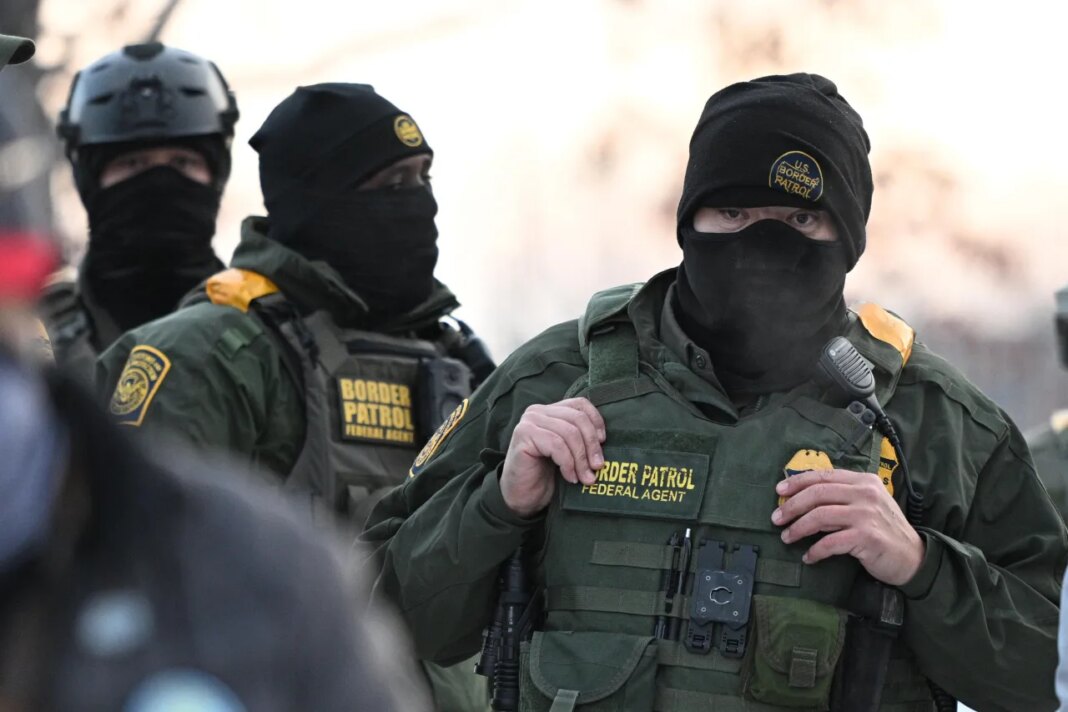 FILE - Federal agents look on as protesters gather outside the Bishop Henry Whipple Federal Building, Thursday, Jan. 8, 2026, in Minneapolis, Minn. (AP Photo/Tom Baker, File)