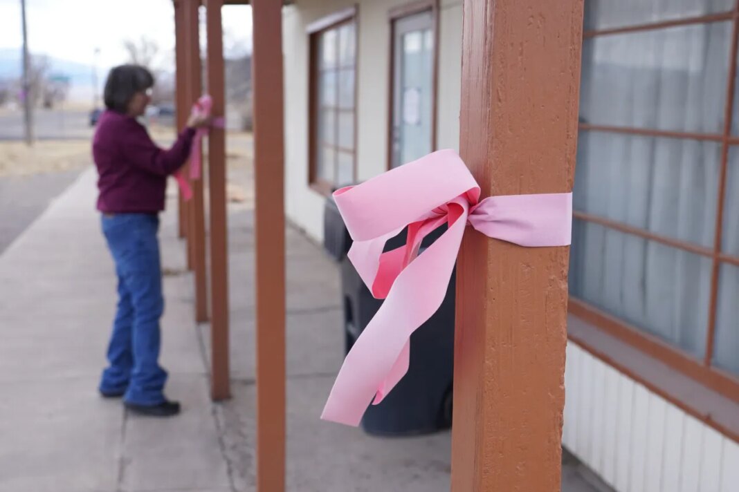A woman hangs a pink ribbon on a pole Thursday, March 5, 2026, in Lyman, Utah, in honor of a woman that was killed a day earlier. (AP Photo/George Frey)