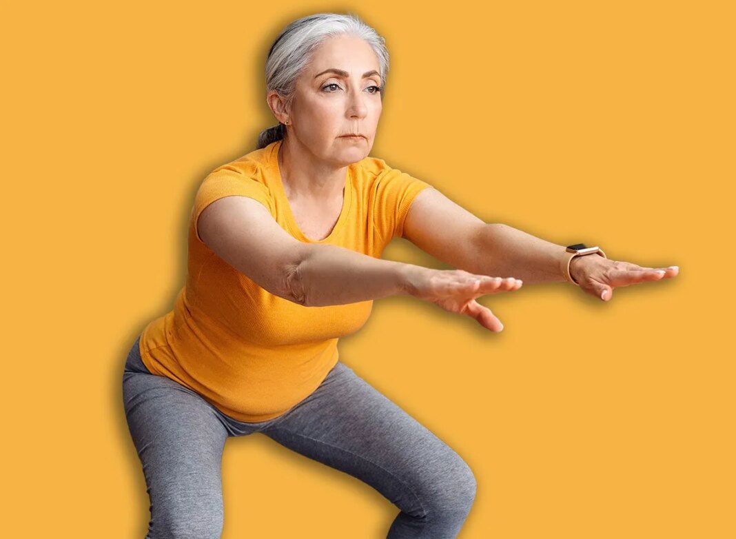 Home workout. Senior lady doing squats on yoga mat, working out at home in living room interior, free space. Fit aged woman exercising her legs on domestic training