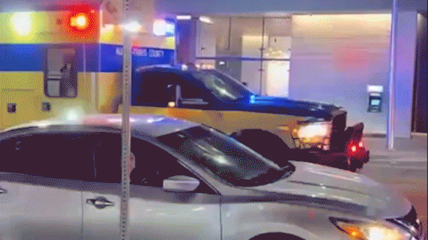 A Waymo autonomous car pauses near an emergency vehicle with flashing lights outside a downtown Austin garage at night.